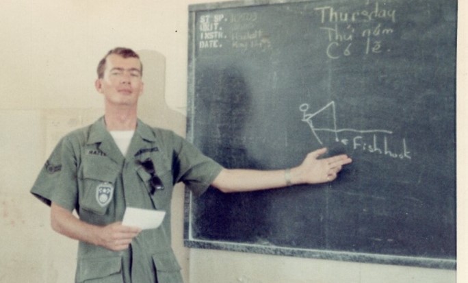 Kirk standing in front of a blackboard in uniform gesturing at writing
