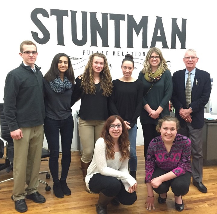Group of students posing with their adviser in front of a public relations agency's sign